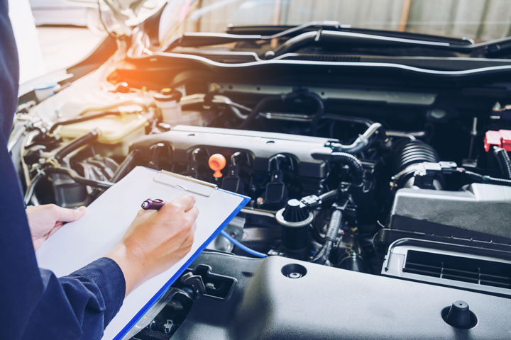 Mechanic holding clipboard with open car engine